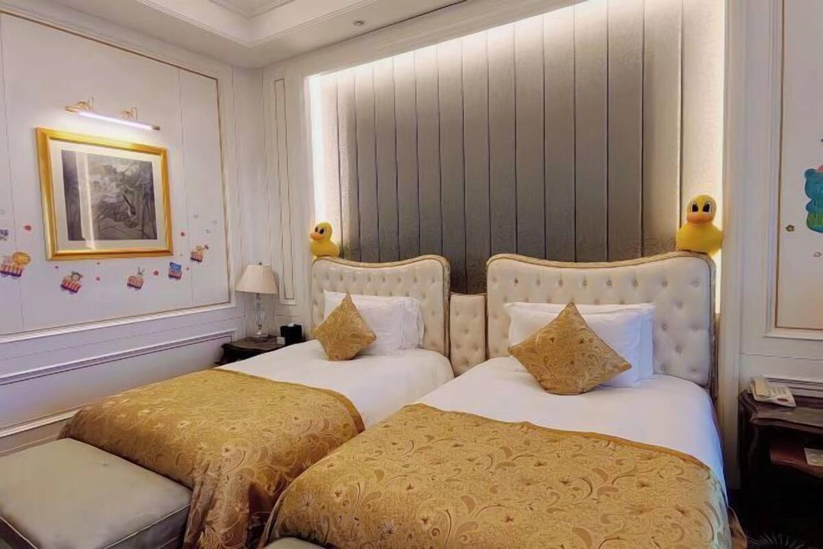 Ein Hotelzimmer mit zwei Betten, jeweils mit Kopfteil, und einer Bank am Fußende der Betten.