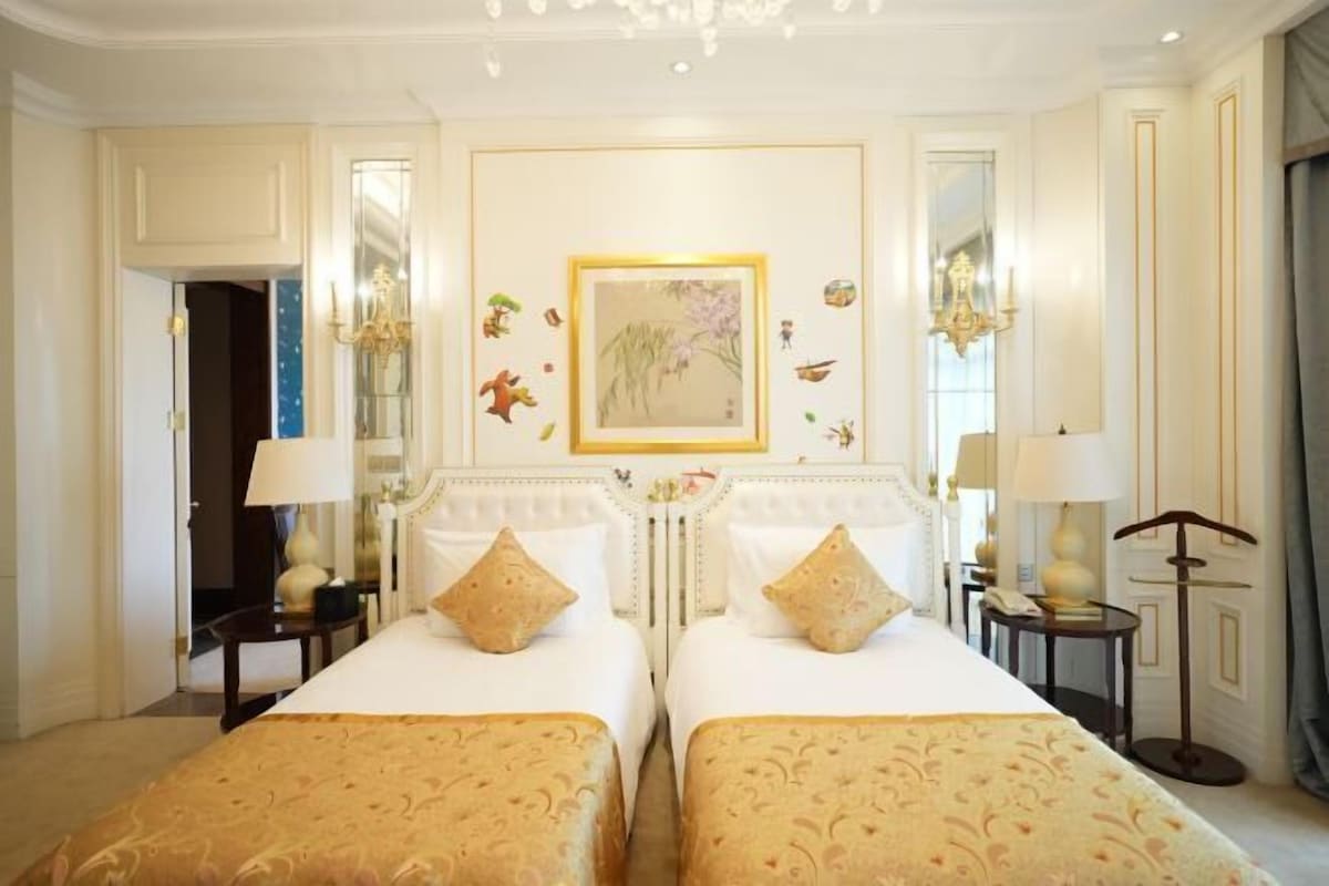 A hotel room with two beds, a chandelier, a painting on the wall, and a mirror.