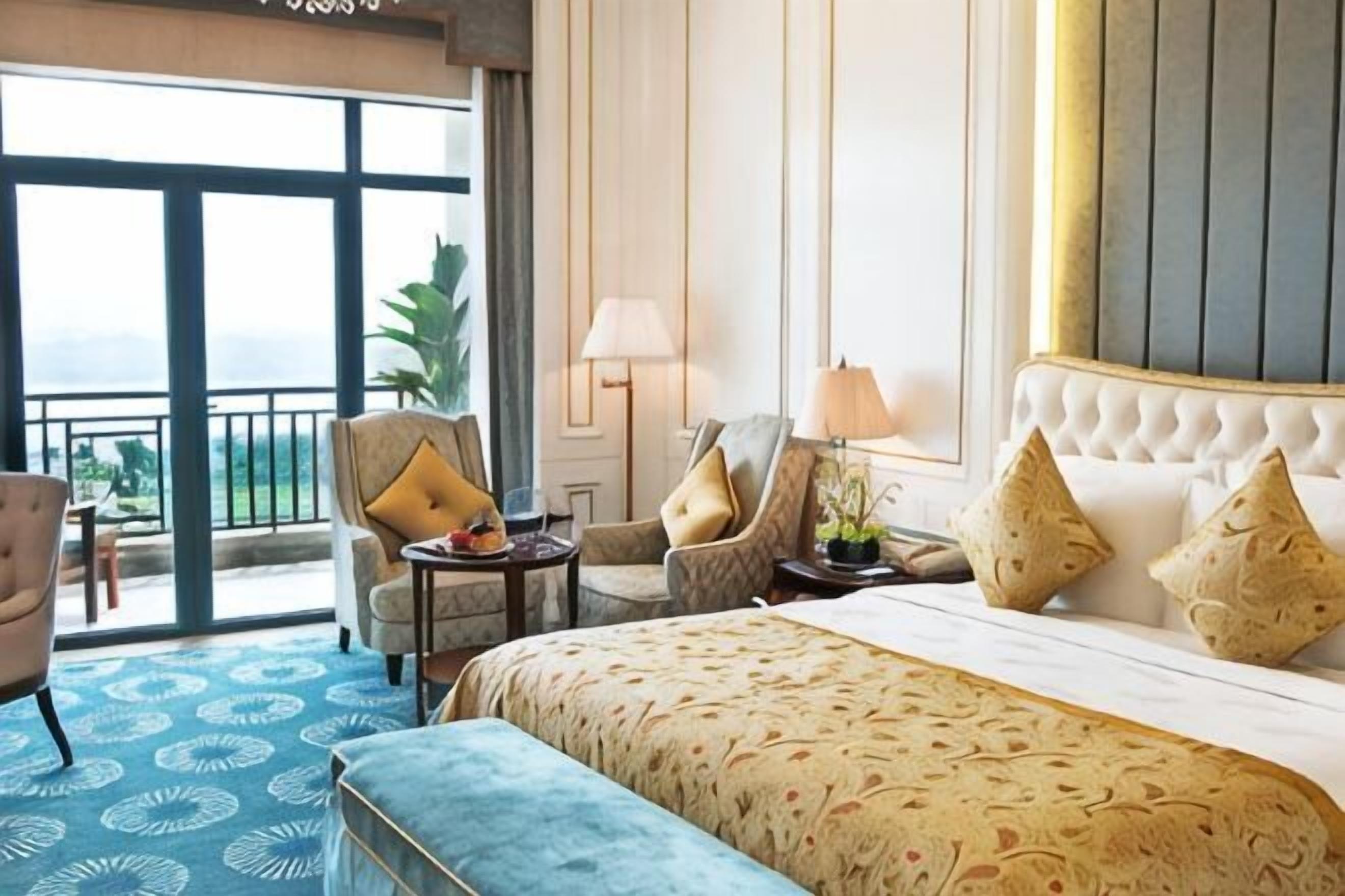 A hotel room with a large bed, two armchairs, a small table, and a balcony with a view.