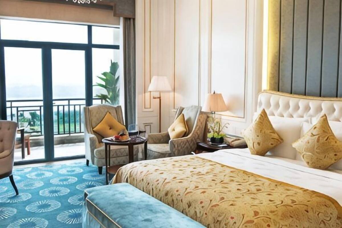 Ein Hotelzimmer mit einem großen Bett, zwei Sesseln, einem kleinen Tisch und einem Balkon mit Blick.