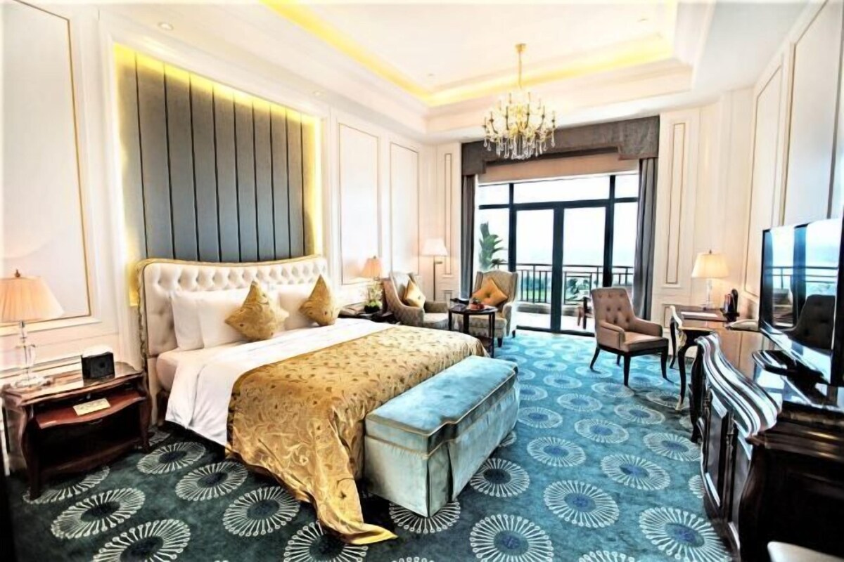 A hotel room with a large bed, a desk, a chair, a TV, and a balcony view.