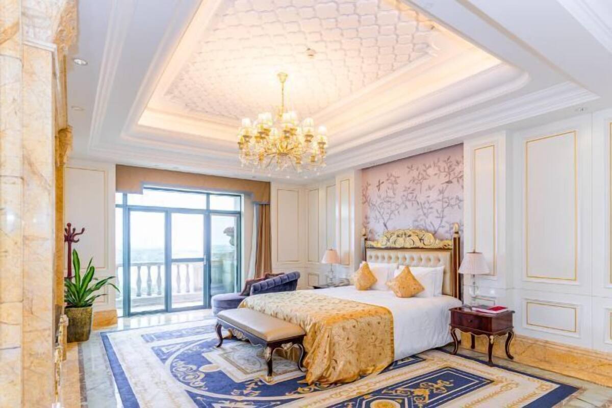 Ein luxuriöses Hotelzimmer mit einem großen Bett, einer Kristallleuchter, einem Balkonblick und aufwendiger Ausstattung.