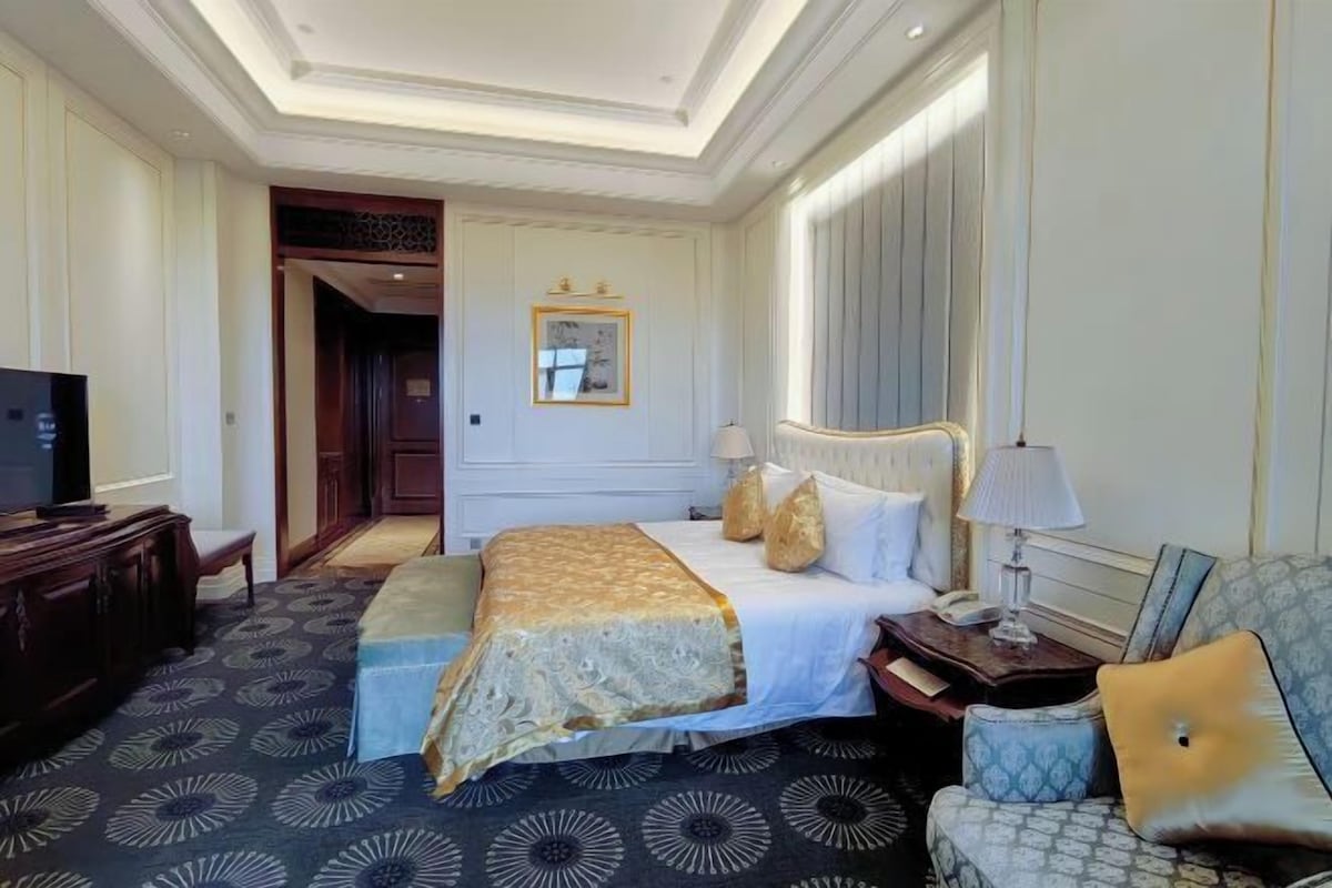 A hotel room with a large bed, a television, a desk, and a sofa.
