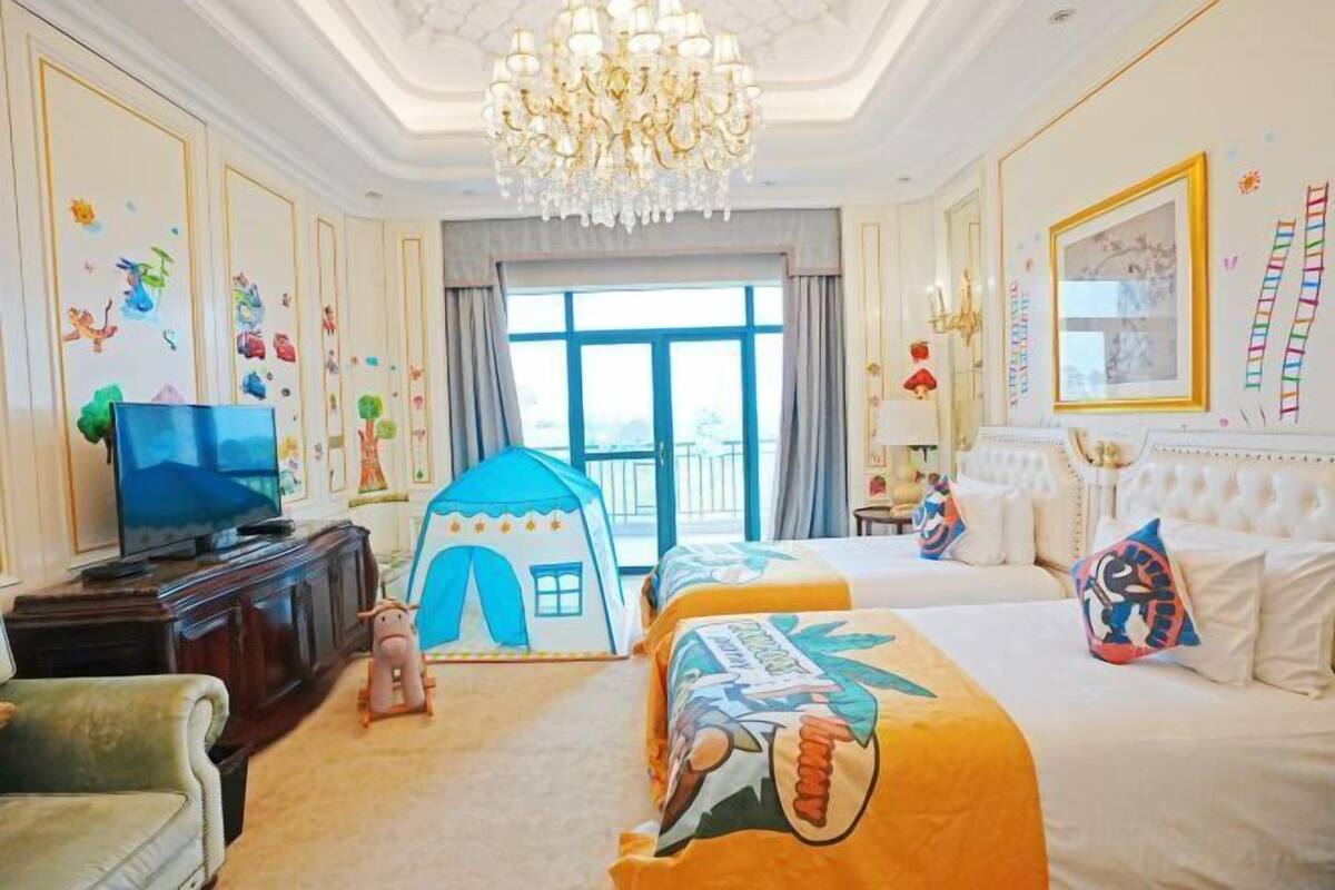 Ein Hotelzimmer mit einem großen Bett, einem kleineren Bett, einem Fernseher, einer Kristallleuchtre und einer zeltartigen Spielzone.