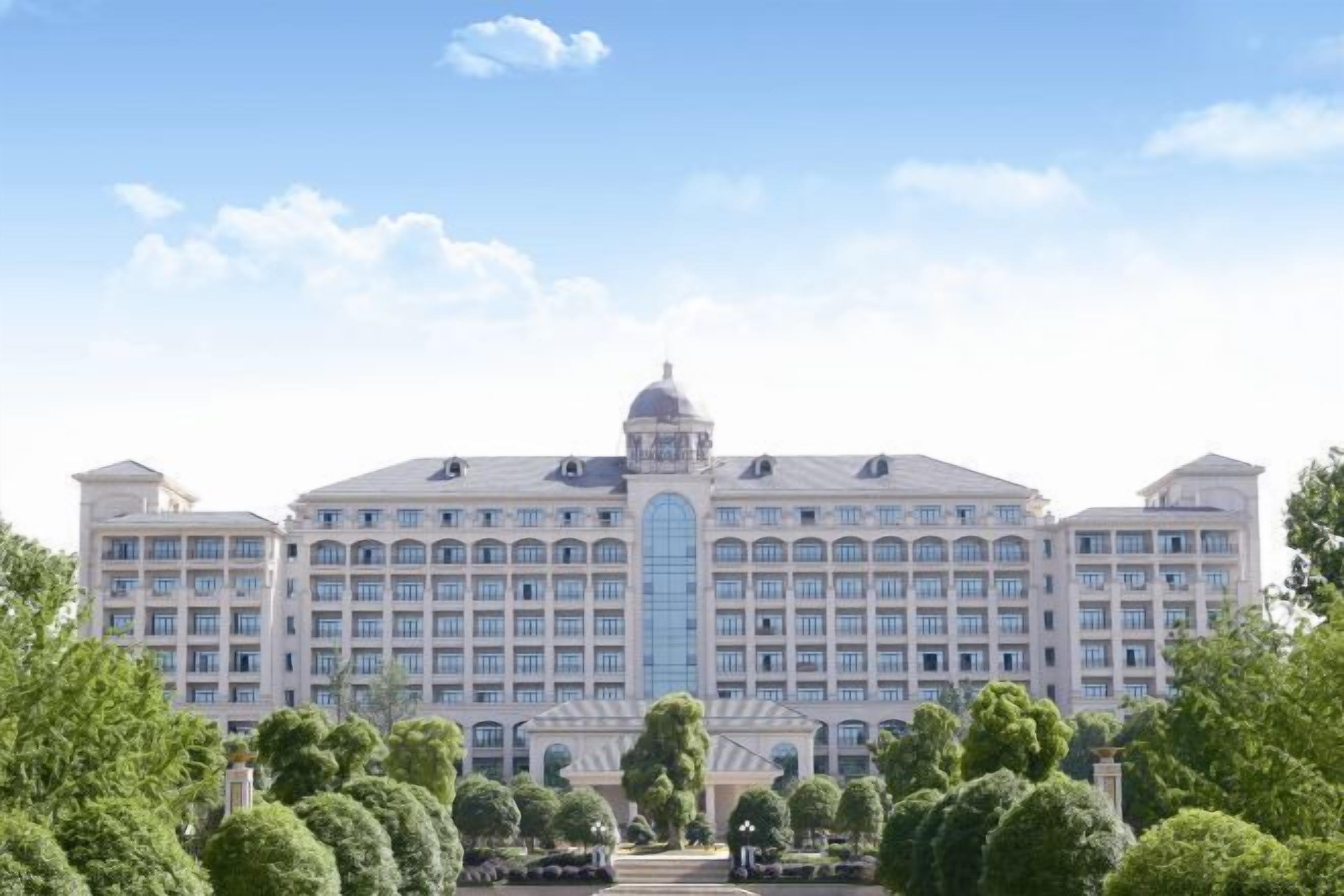 A large, multi-story hotel with a central dome and symmetrical wings, surrounded by well-maintained trees.