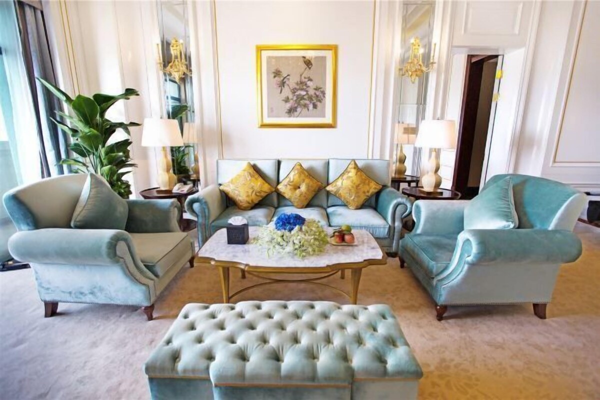A room with a light blue sofa set, a tufted ottoman, a coffee table, and a framed floral artwork on the wall.