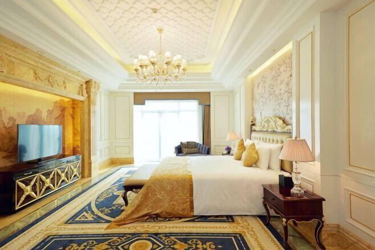 Ein Hotelzimmer mit einem großen Bett, einem Fernseher, einer Kristallleuchtre und einem gemusterten Teppich.