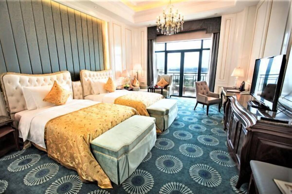 Ein Hotelzimmer mit zwei Betten, einem Balkon, einem Fernseher und einer Kristallleuchter.
