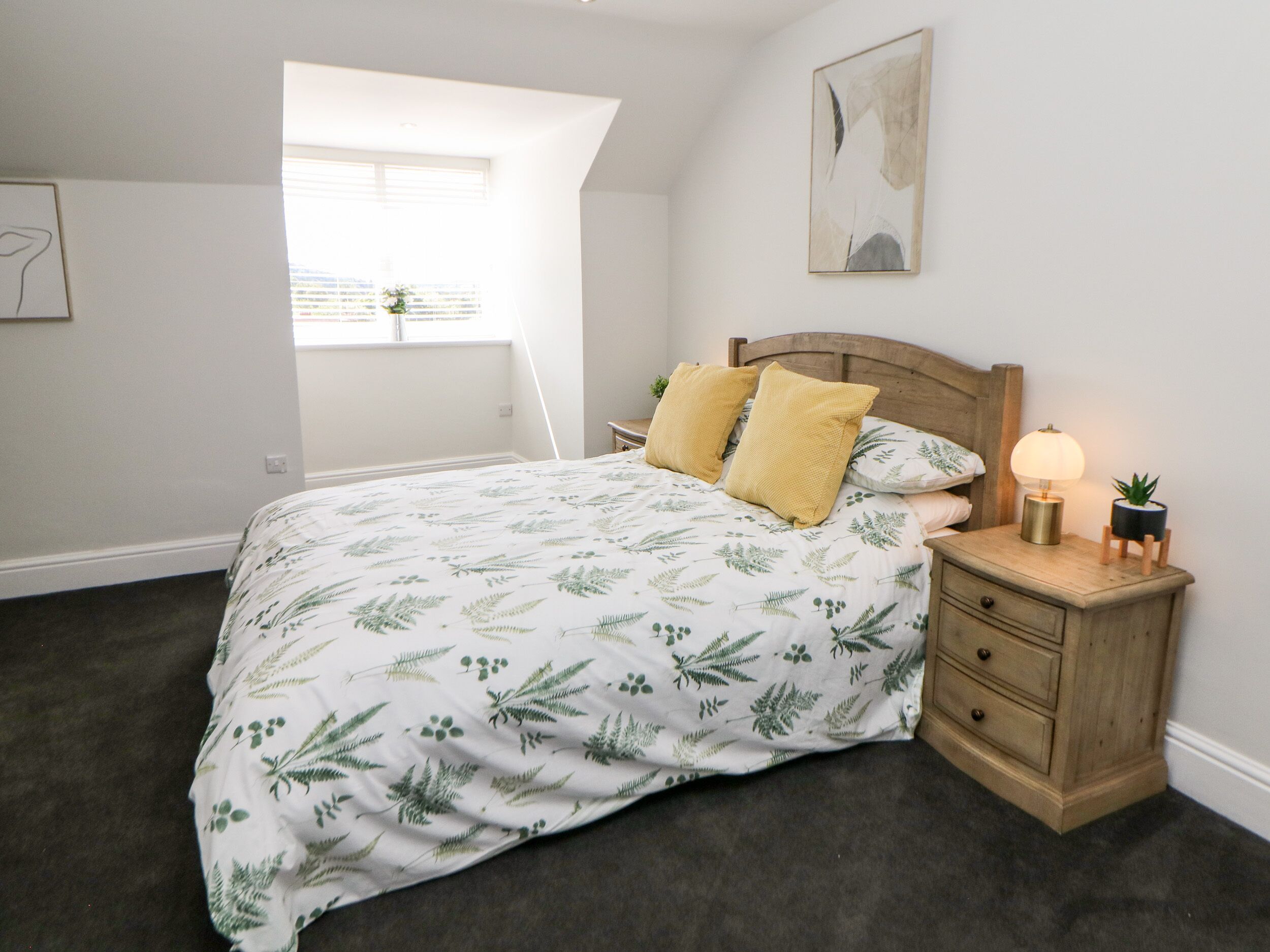 A bedroom with a bed, a nightstand, a lamp, and a window.