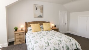A bedroom with a large bed, two bedside tables with lamps, a door, and a ceiling light. - Sunshine Apartment (Belper)
