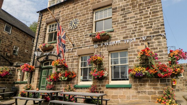 A stone building with a flag, flower baskets, and outdoor seating. - Sunshine Apartment (Belper)