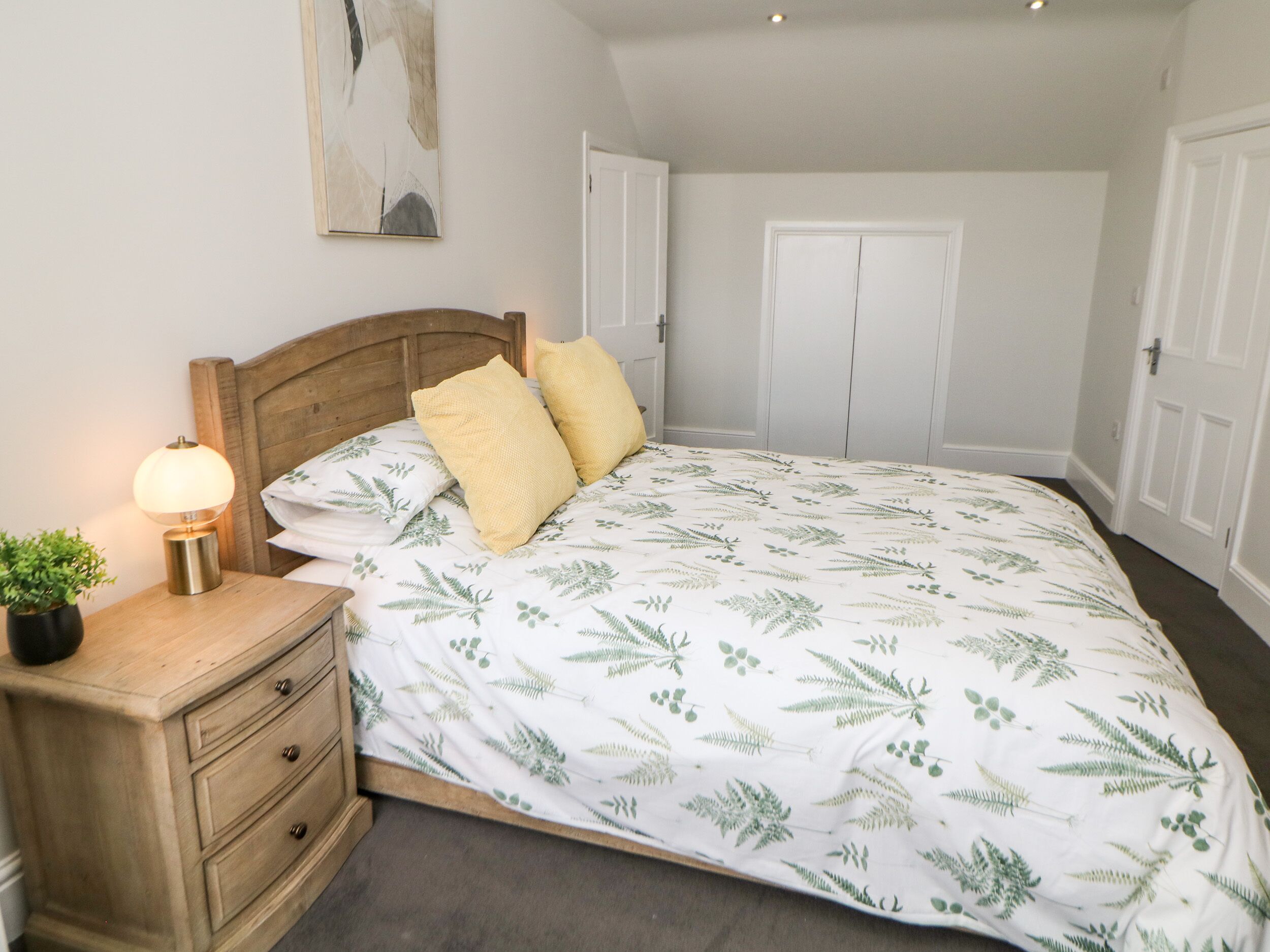 Un dormitorio con cama, mesita de noche, lámpara y una planta.