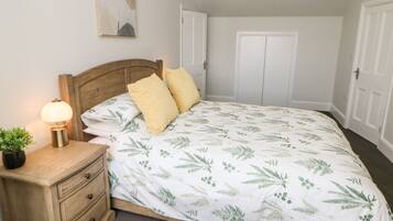 A bedroom with a bed, bedside table, lamp, and a plant.