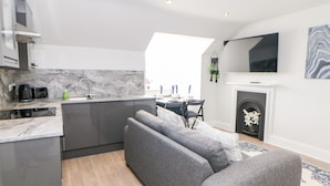 A modern kitchen with a built-in island, grey sofa, and a fireplace. - Sunshine Apartment (Belper)