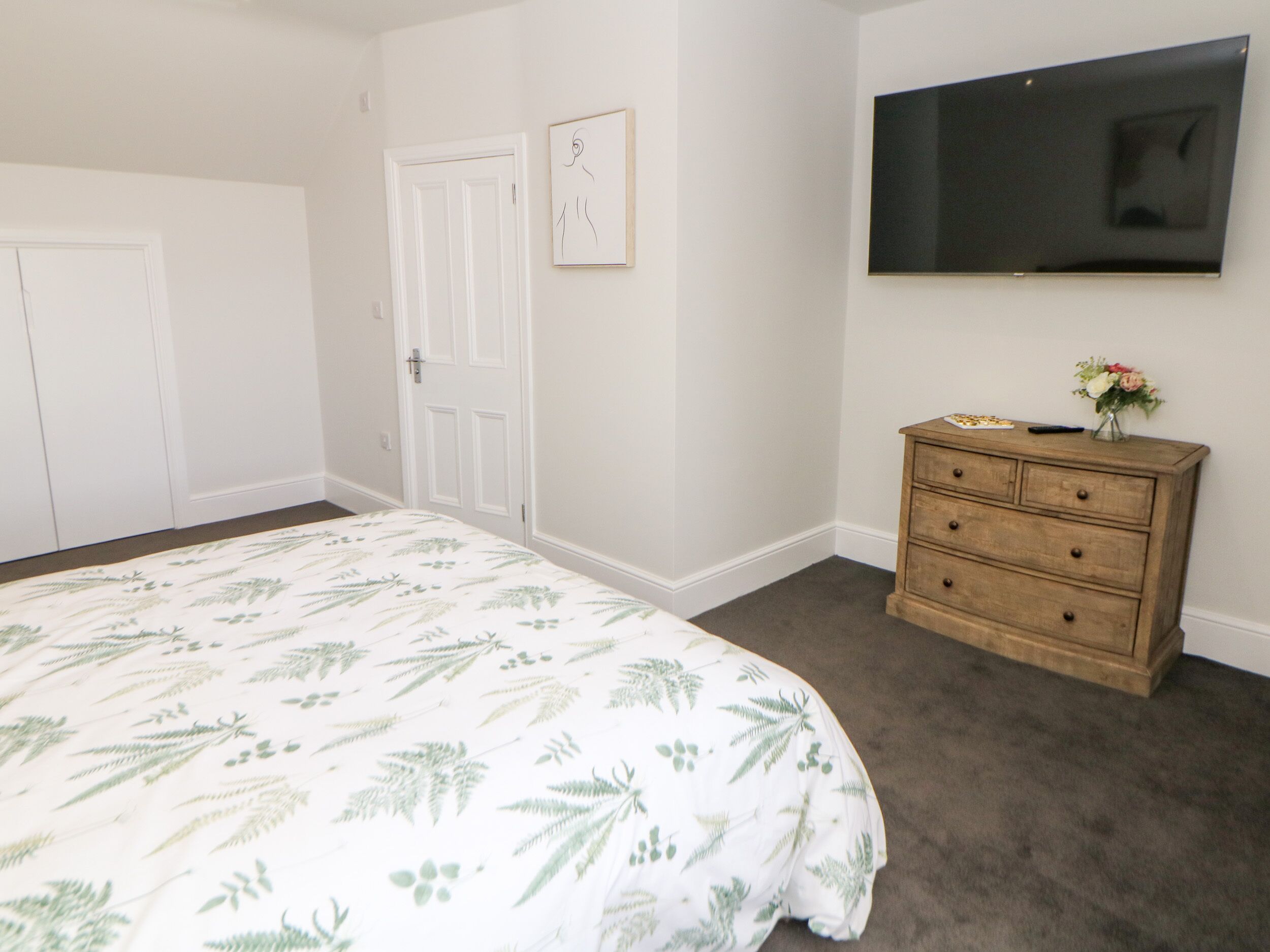 Un dormitorio con cama, cómoda, televisor y dos puertas.