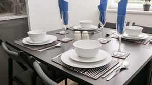 A dining table set with white plates, bowls, and cutlery, with blue napkins folded on the table. - Sunshine Apartment (Belper)