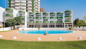 Ein modernes Hotel mit einem zentral gelegenen Schwimmbad, mehreren Balkonen und einem gepflegten Rasen.