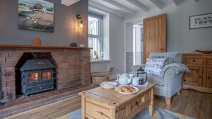 A cozy living room with a brick fireplace, wooden furniture, and a view of the outside. - Wern Y Glais - 2 Bedroom Cottage - Glais (Swansea)