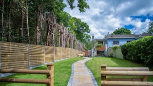 A pathway leading to a house with a blue exterior, surrounded by a wooden fence and lush greenery. - Wern Y Glais - 2 Bedroom Cottage - Glais (Swansea)