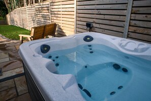 A hot tub with multiple jets, a wooden chair, and a wooden fence in the background.