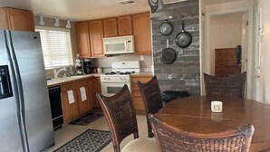 Una cocina con armarios de madera, un refrigerador de acero inoxidable, un microondas blanco, una estufa y una mesa de comedor con cuatro sillas.