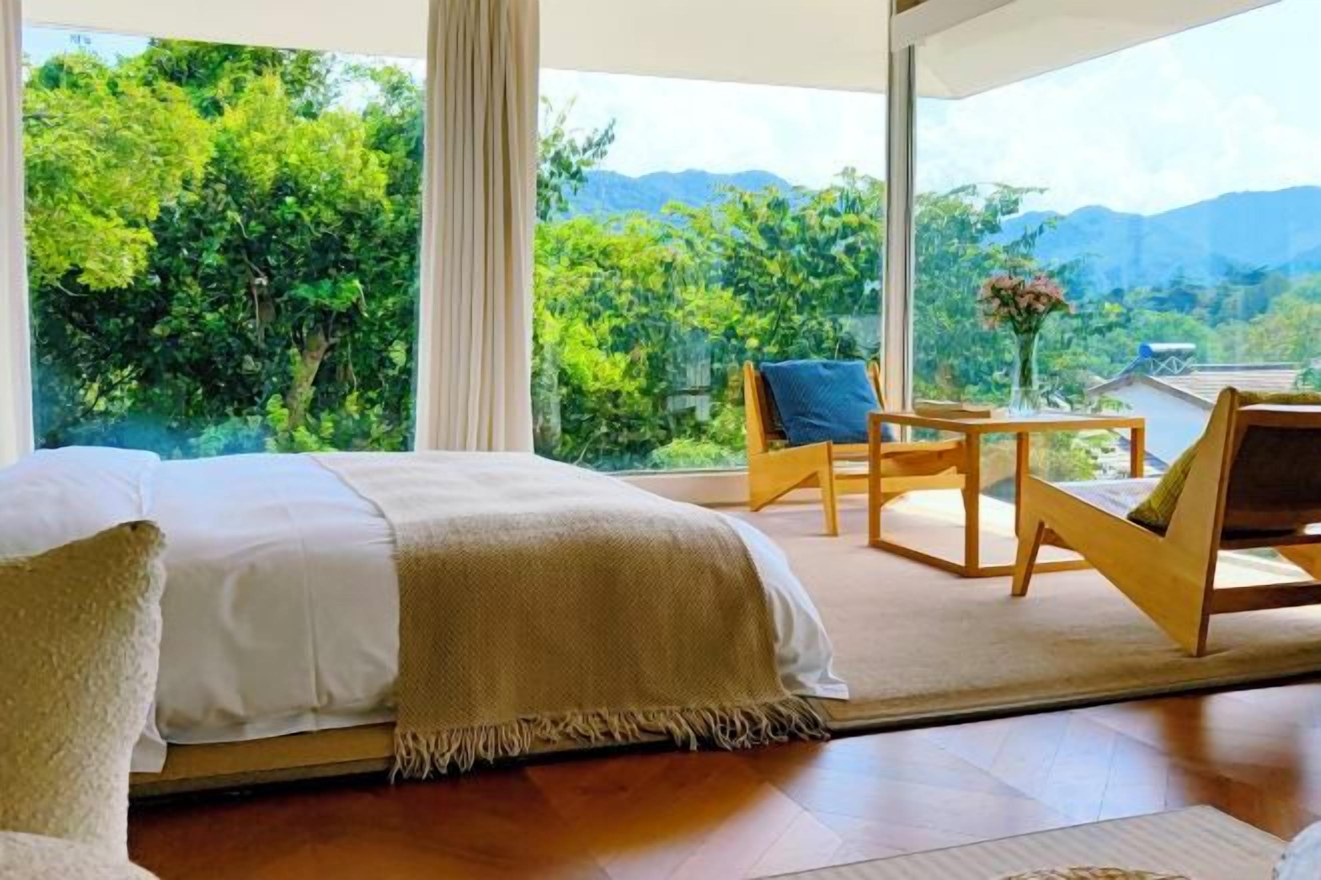 Un dormitorio con una cama grande, una mesa de madera y sillas, y vistas a la exuberante vegetación y montañas.