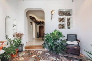 A hallway with a patterned floor, a seating area with a chair, and a staircase leading to another level.