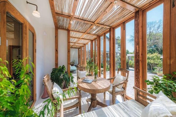 Una habitación iluminada por el sol, con techo de madera, ventanas amplias y una mesa redonda con sillas.
