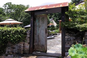 A rustic wooden gate with a metal roof, leading to a paved pathway.