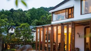 Moderni talo, jossa on suuri lasiovi, kivinen patsas ja näkymä metsäiselle kukkulalle.