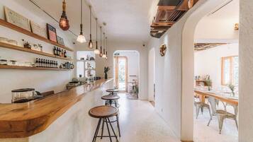 Zona de bar con taburetes, estanterías llenas de botellas y luces colgantes.