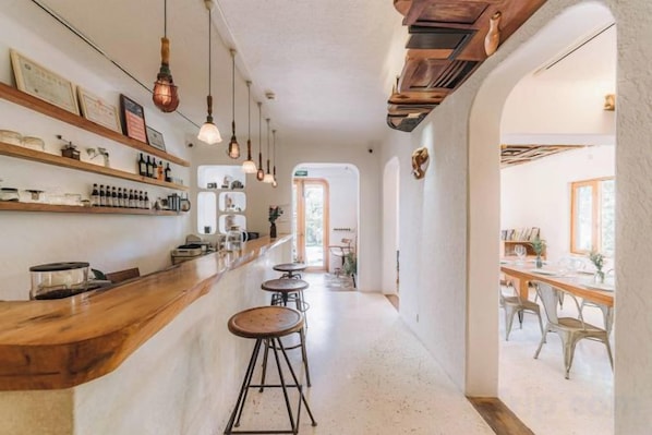 A bar area with stools, shelves with bottles, and hanging lights.