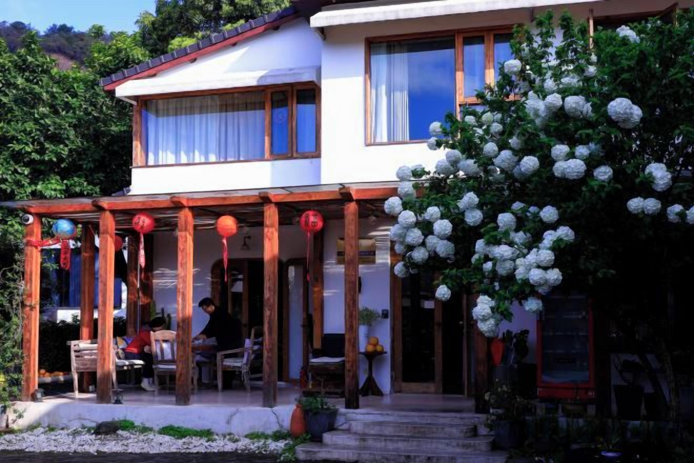 Un edificio di due piani con un portico coperto e un giardino con fiori bianchi.