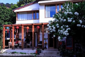 A two-story building with a covered porch and a garden with white flowers.