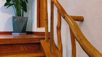 Una escalera de madera con barandilla, una planta en maceta en el rellano y una pared blanca.