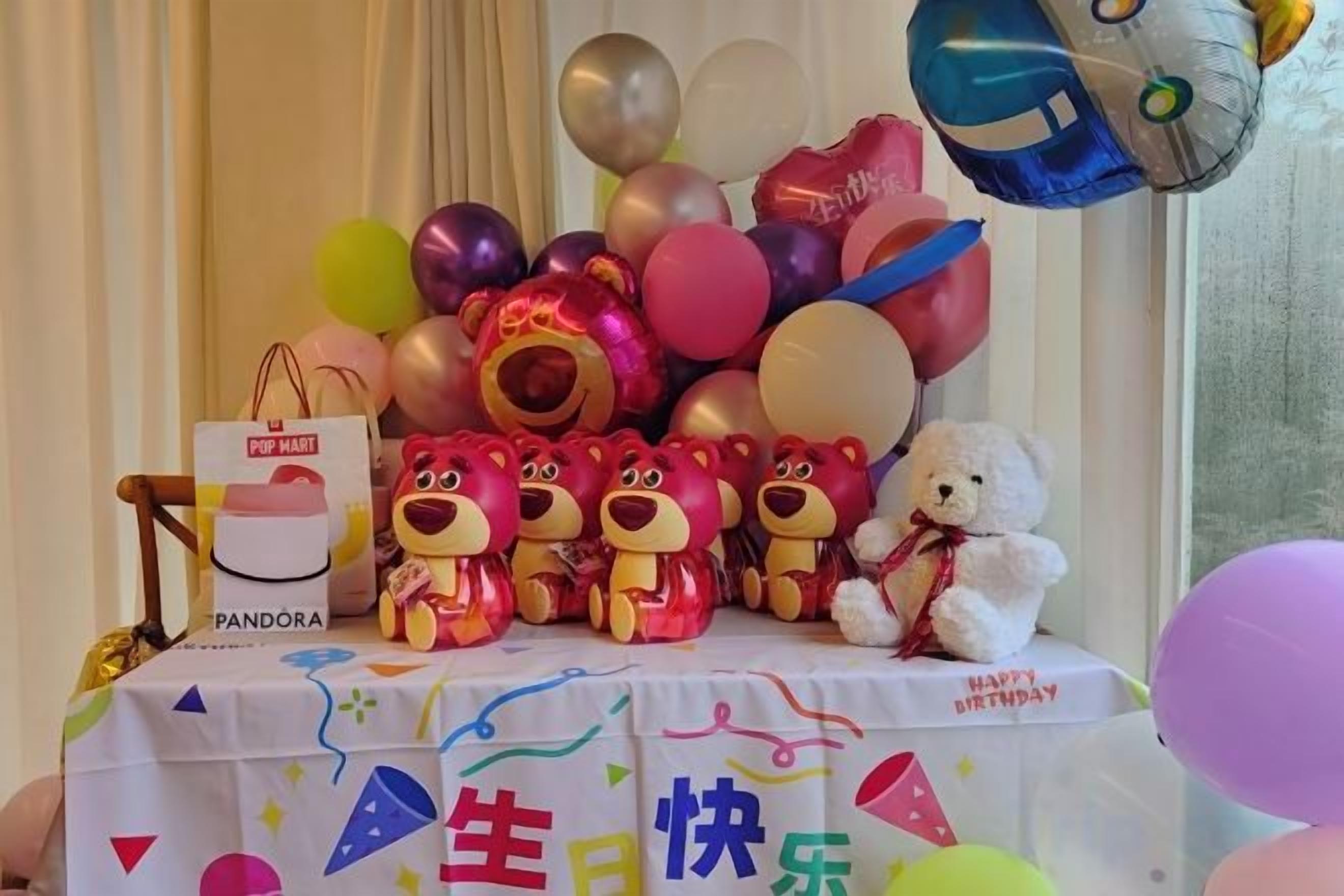 Una mesa con globos, un osito de peluche y una caja de regalo.