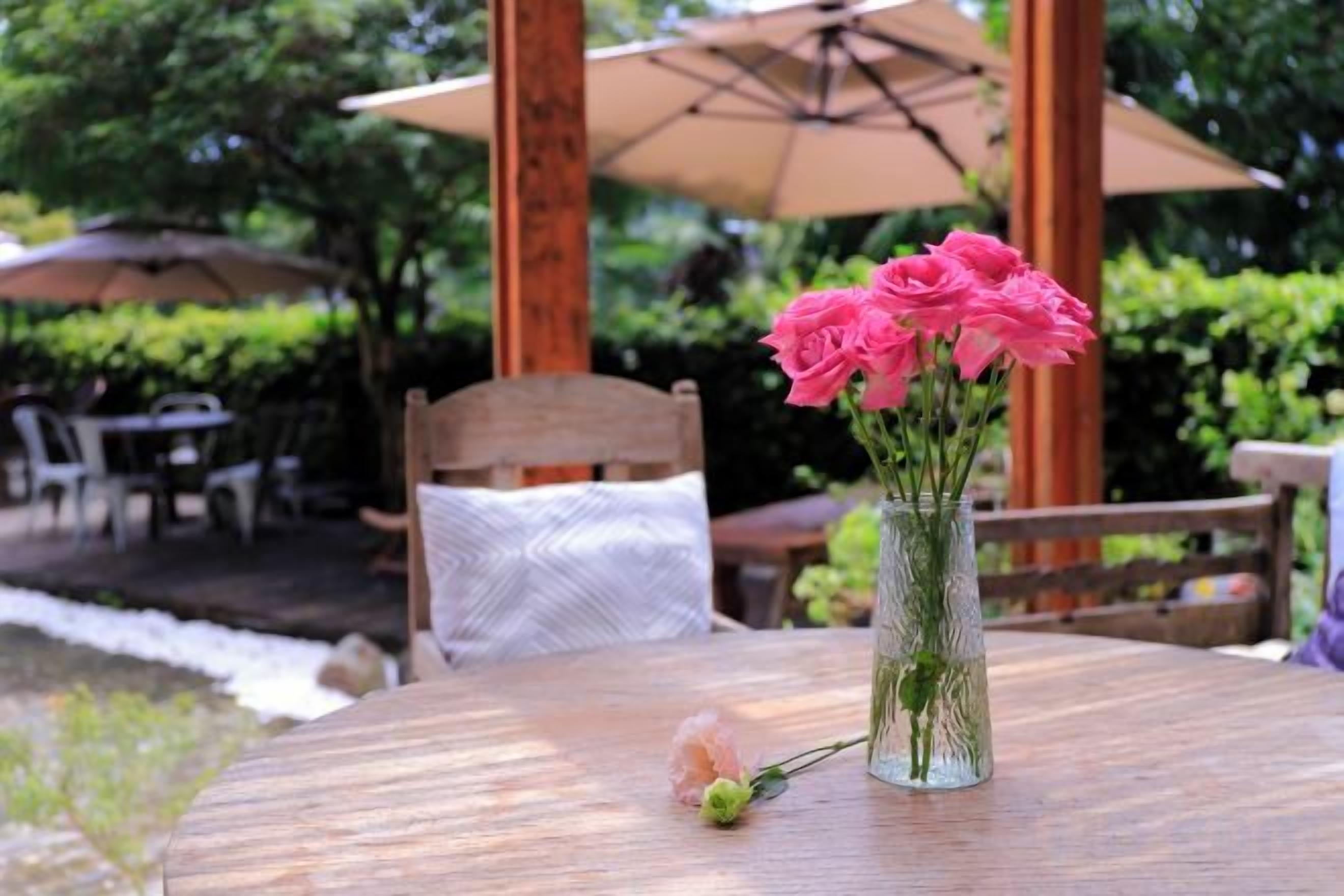 A wooden table with a clear glass vase containing pink flowers.