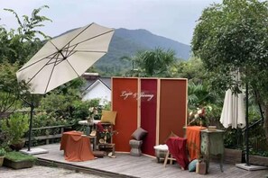 Ein gemütlicher Außenbereich mit einer Holzterrasse, einer roten Wand mit dem Schriftzug 'Lijia & Jiang' und einem großen Sonnenschirm, der Schatten spendet.