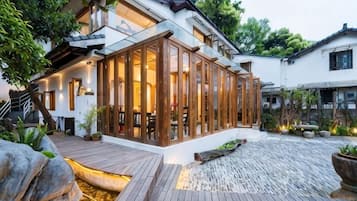 Una casa moderna con un amplio ventanal de vidrio, una terraza de madera y un estanque de carpas.