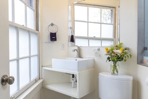 A bathroom with a white sink, a toilet, a window, and a vase with flowers. - Deluxe Queen Room with View and Ensuite Bath (San Francisco)