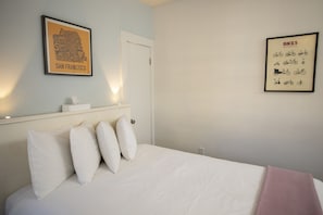 Une chambre à coucher avec un lit, des oreillers, une carte encadrée de San Francisco et une illustration encadrée représentant un vélo.