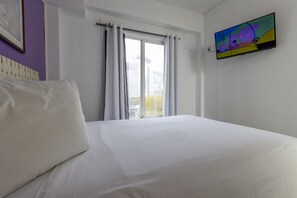 Ein Hotelzimmer mit Bett, Fenster mit Vorhängen und Fernseher an der Wand.