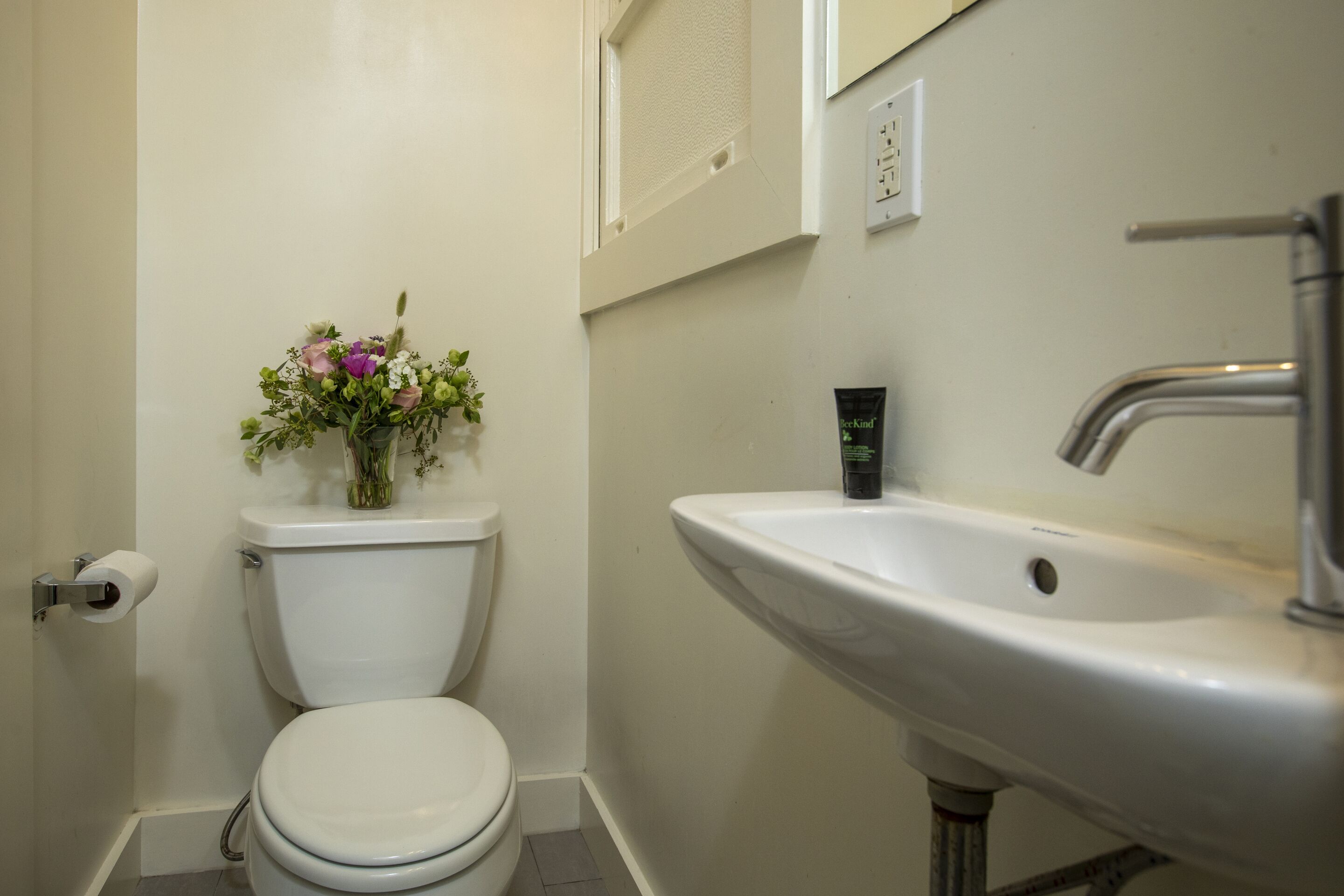 Un baño con inodoro, lavamanos y un pequeño jarrón con flores.
