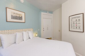 A hotel room with a bed, a framed cityscape picture, a framed bear guide, and a door.