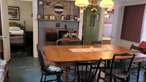 A dining area with a wooden table and chairs, a fireplace, and a clock on the wall. - Quaint quarters in South Wellfleet (Wellfleet)