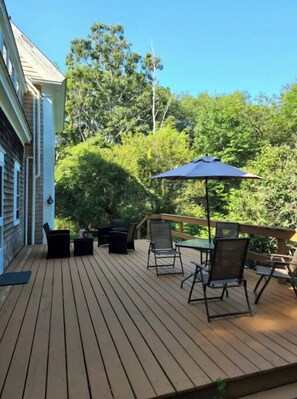 Une terrasse en bois avec des meubles d’extérieur et une table placée sous un parasol bleu.