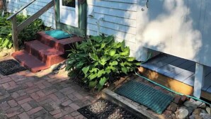 A house with a front porch, steps leading to the door, and a small garden area with plants and a doormat. - Quaint quarters in South Wellfleet (Wellfleet)