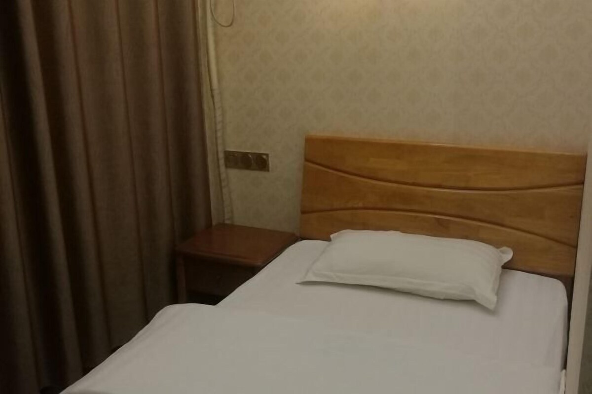 A single bed with a wooden headboard, a white pillow, and a wooden nightstand beside it.