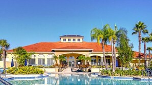 A hotel with a swimming pool, palm trees, and a red-tiled roof.