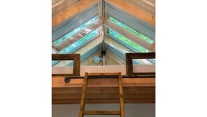 Een dakraam met een houten ladder die naar een plafondventilator leidt.